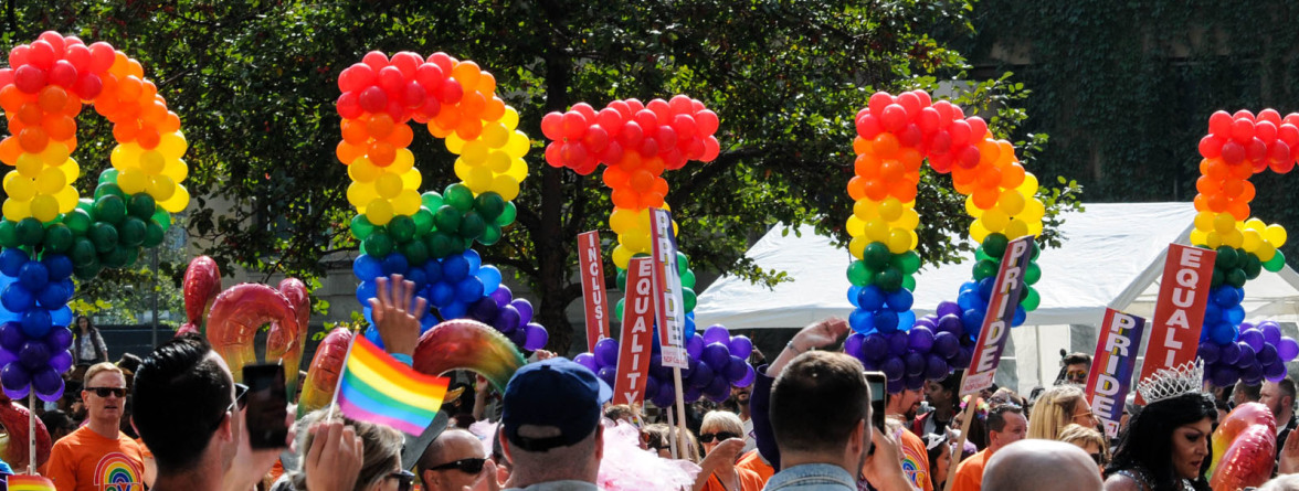 A group of LGBT people holding multi-colored PRIDE balloons