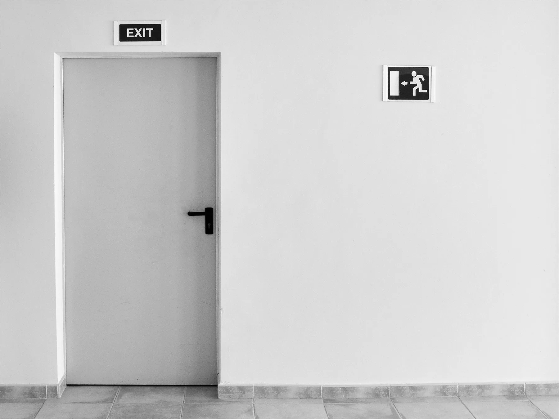 An image of a white wall with an exit door and a sign above it.
