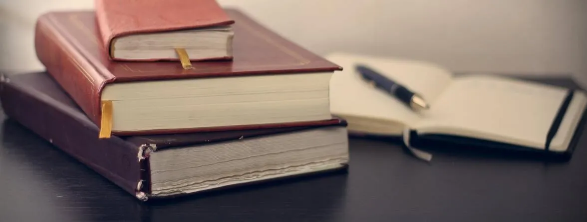 An image of a notebook that is filed and another that is open, with a pen on top.