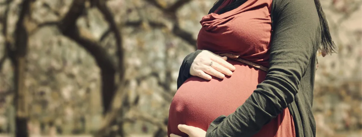 An image of a pregnant woman holding her large belly against a blurred background