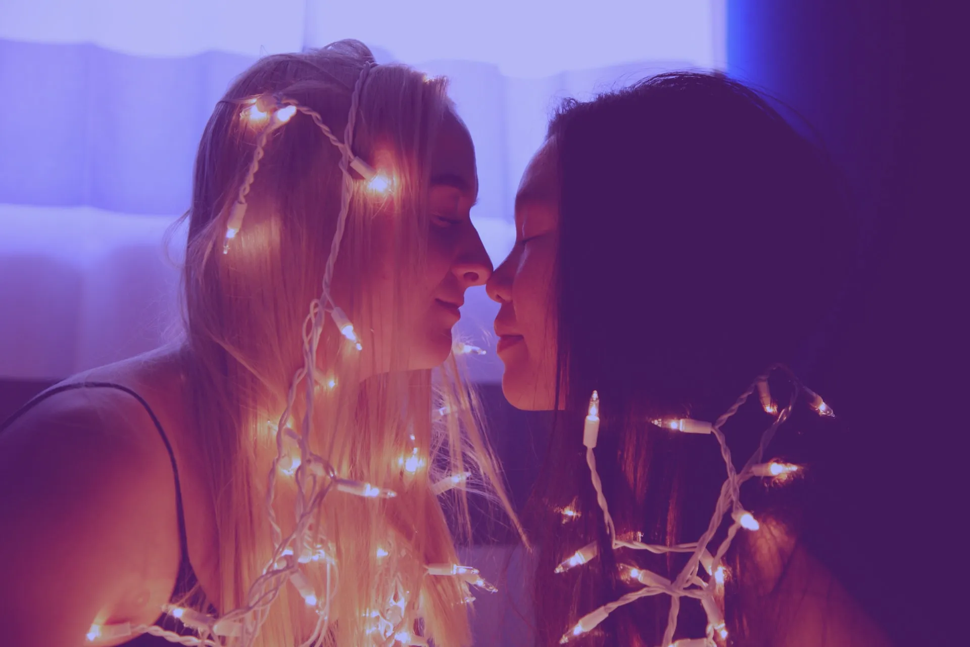 Two girls wearing lights in their hair, touching noses