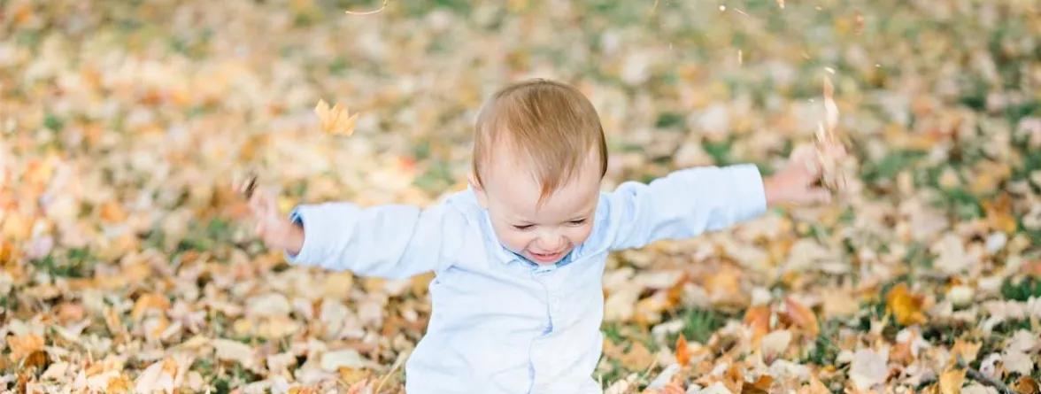 A baby with open arms playing outside.