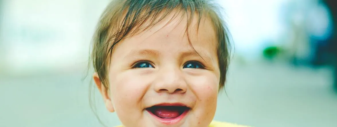 A baby girl with a pretty smile in a blurry background.