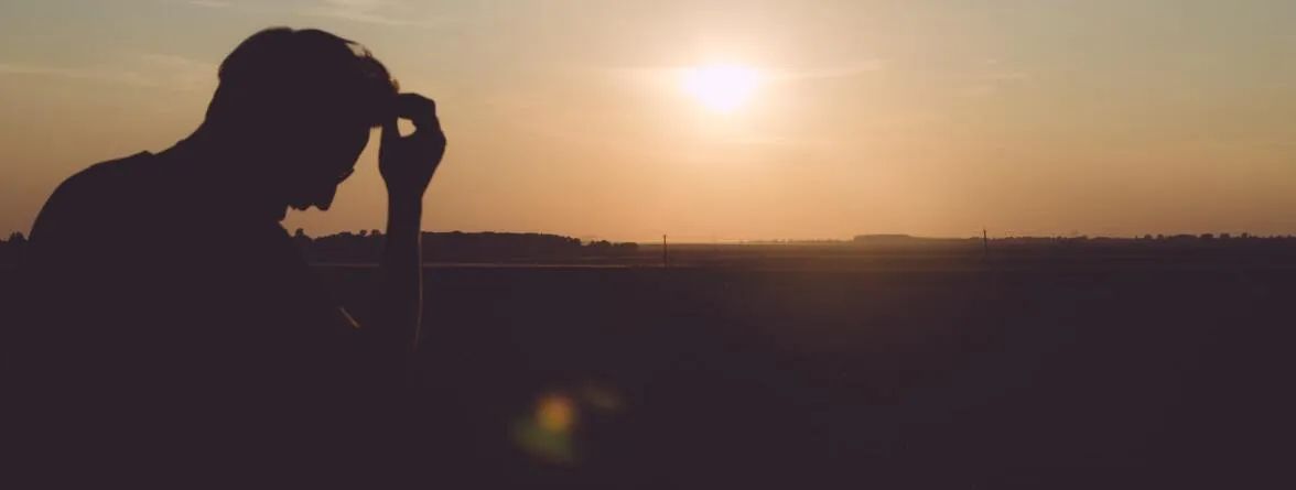An image of a man holding his head and looking down under the sunset.”