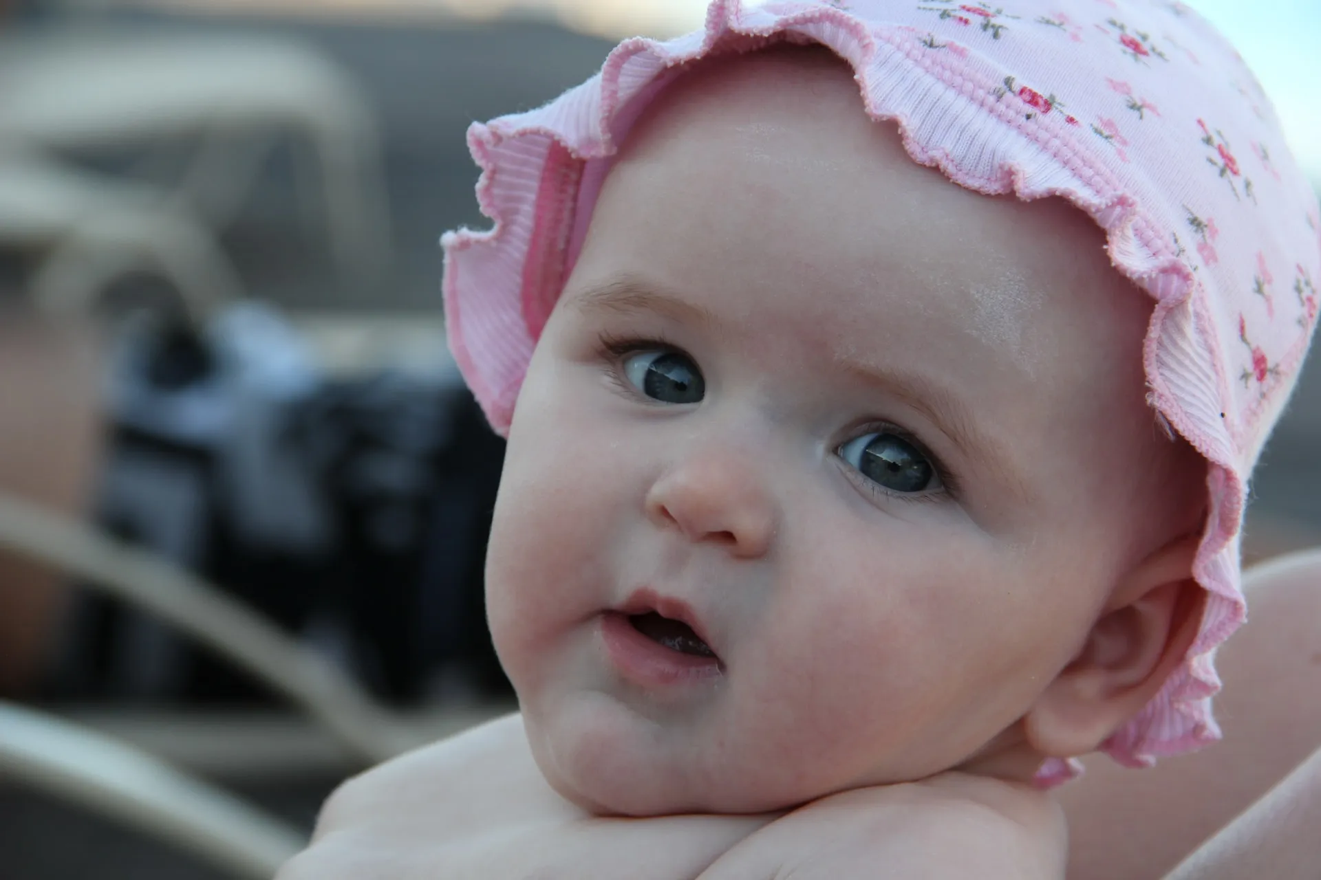 An image of a beautiful baby girl facing forward and wearing a pink cap