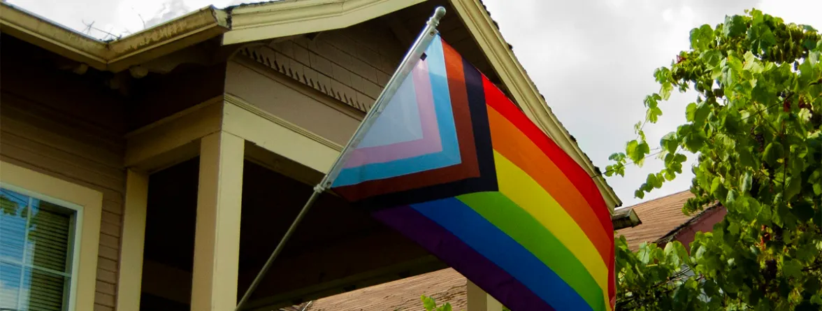 A colorful flag is displayed outside the house, surrounded by green leaves
