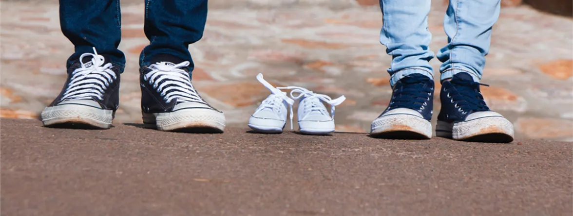 Two pairs of legs with a single pair of shoes placed between them.