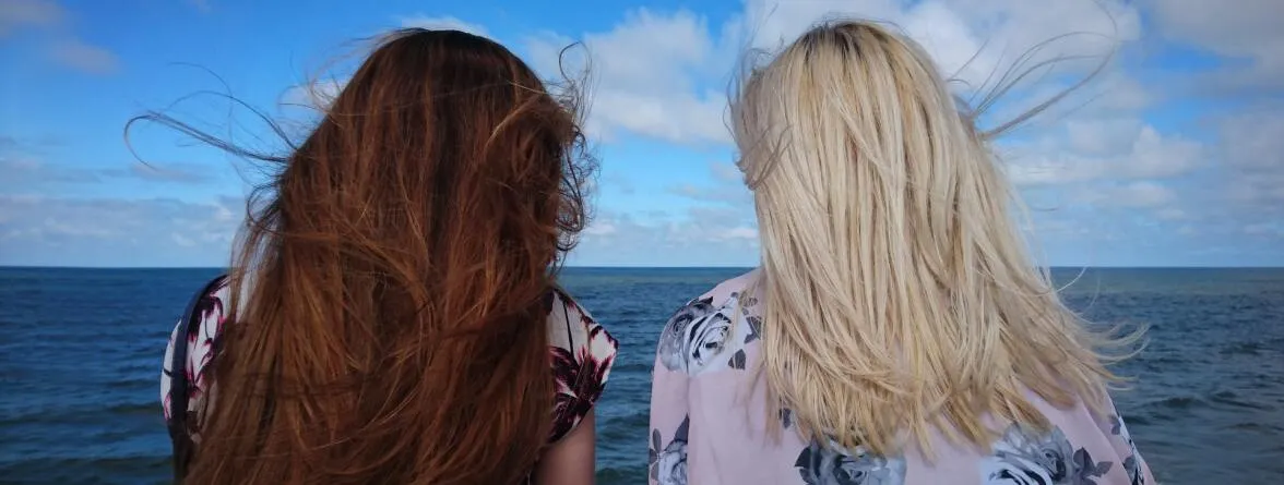 Two girls with their backs turned, facing the sea.
