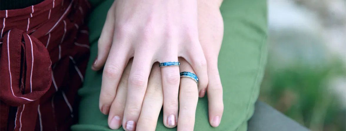 Two hands wearing matching rings, holding each other.