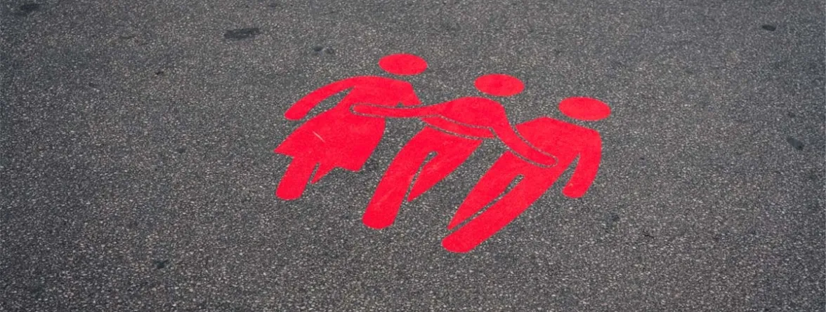 Red painted symbols of three human figures holding hands on pavement, representing gender equality and unity.