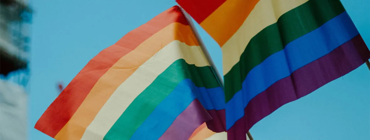 Two rainbow Pride flags waving against a clear blue sky